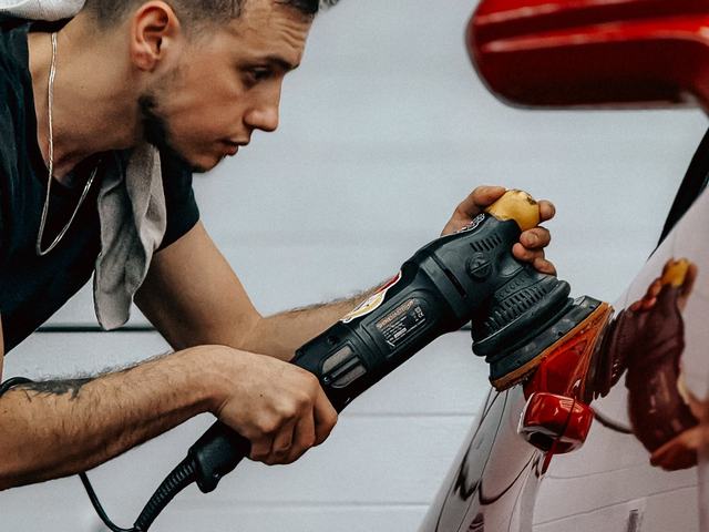 A detailer running a rotary polisher along a red car panel