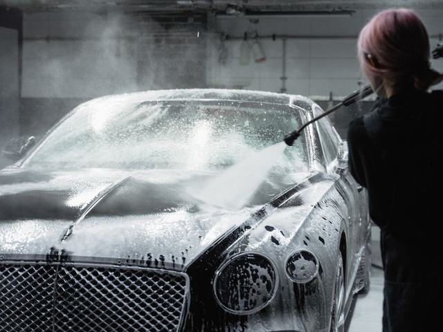 A dark car covered in thick snow foam during a wash