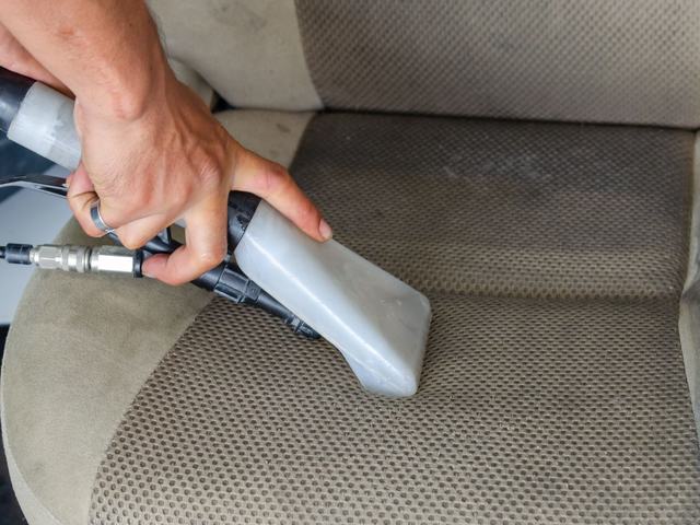 An extractor nozzle deep-cleaning a fabric car seat